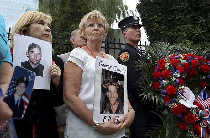 In this Sept. 10, 2011 file photo, Rosemary Cain, center, of Massapequa, N.Y., who lost her son, FDNY firefighter George Cain, while responding to the 9/11 attacks at ground zero, stands with Sally Regenhard, left, who lost her son, FDNY firefighter Christian Regenhard, and FDNY firefighter John Darcy, right, during a wreath laying ceremony to honor of over 6,000 human remains of their loved ones which are housed in a temporary structure at Memorial Park in New York. 