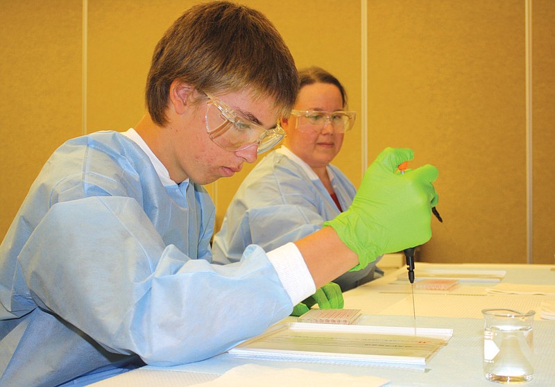  Fulton High School student Brian McCarty, 16, practices testing for sickle cell disease using red food coloring while (back) Carlene Campbell, newborn screening supervisor, explains how laboratory scientists go through the real process. 
