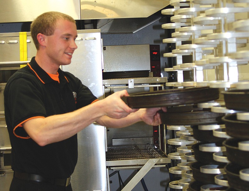 Tyler Gilleland, manager of the Fulton Little Caesars, pulls pizzas off the rack inside of the Love Kitchen. The Love Kitchen is a mobile unit that travels across the U.S. serving pizzas to the hungry. The unit stopped at the Fulton Soup Kitchen Wednesday.