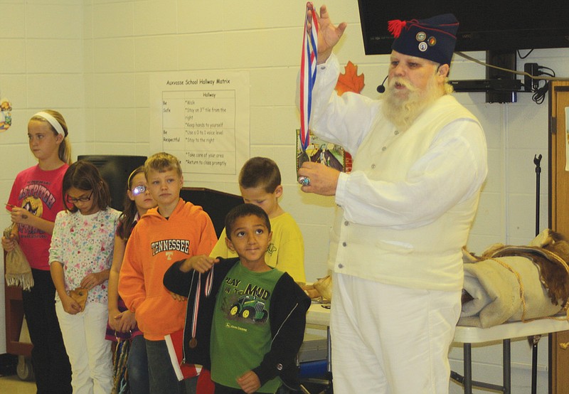 First-grader Matthew Weber holds a medal for Jim Two Crows Wallen, oral historian, Tuesday at Auxvasse Elementary School. Wallen had a few students help out during his presentation of Lewis and Clark's expedition.