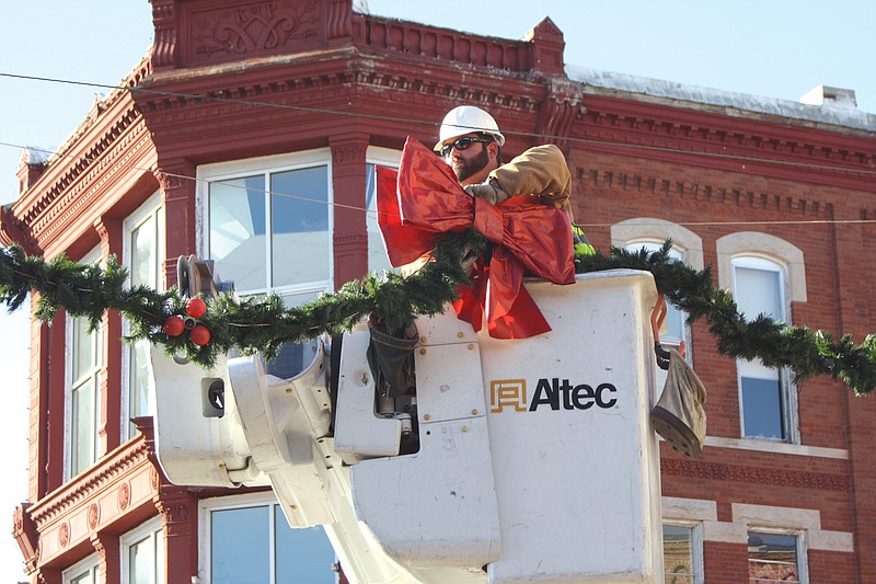 Patrick Craighead, lineman for the City of Fulton, places a bow on a garland that stretches across Court Street. City workers were out bright and early Thursday morning decorating the downtown area for Christmas.