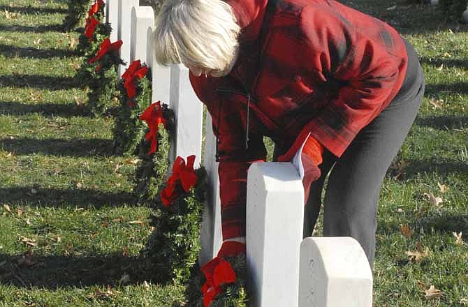 Judy Voigt helps to secure the wreaths in the ground during the "Wreaths For Heroes" event at the National Cemetery on Saturday morning in Jefferson City, where volunteers placed 1,587 wreaths. Voigt has two sons serving in the military, so this event is dear to her heart. 