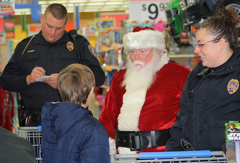 Logan Smith of Millersburg, a student at McIntire Elementary School, tells Santa he also bought a doll for a friend who is paralyzed in a hospital. He was shopping during t he annual Shop With A Cop event at the Fulton Walmart. Helping Logan shop is Mackenzie Elmore, A Fulton DARE officer. At left is Fulton Police Officer Lance Reams.