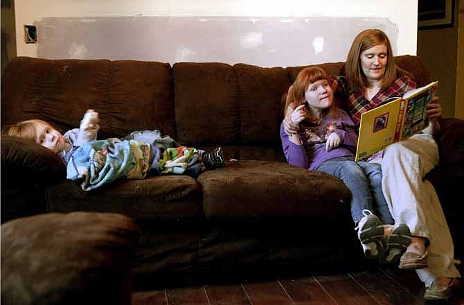 As Lindsey Scholar reads a book to her daughter Taylor, 11, who suffers brain damage from Shaken Baby Syndrome, brother Landon lays down while playing a video game with the controller in his hands Dec. 6, 2011, in Moorhead, Minn. Marks on the wall are from a construction project to make a bathroom wheelchair accessible. (AP Photo/Dave Wallis, The Forum)