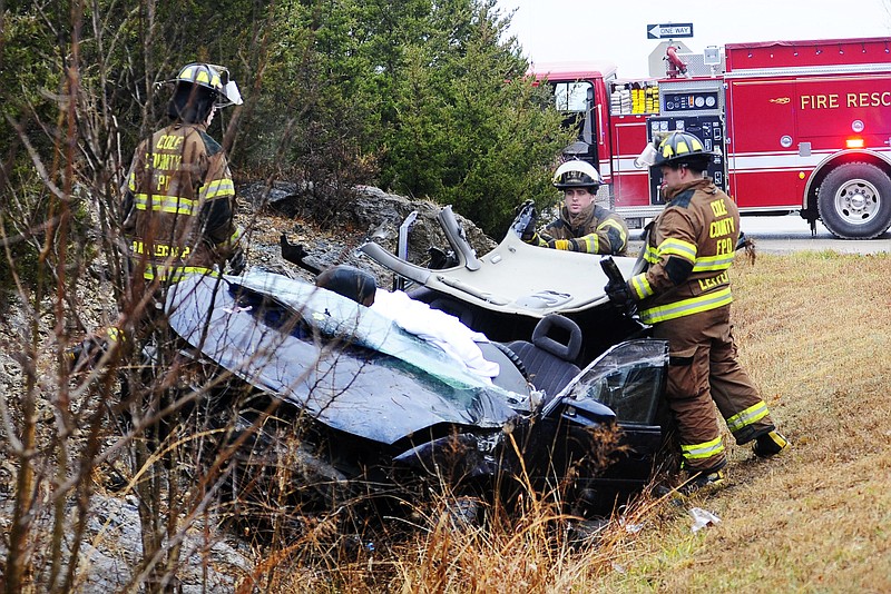 Firefighters from the Cole County Fire Protection District gather pieces of a 2002 Pontiac Gran Prix that hit a rock bluff Tuesday morning on Brown Road near the intersection with U.S. 54.