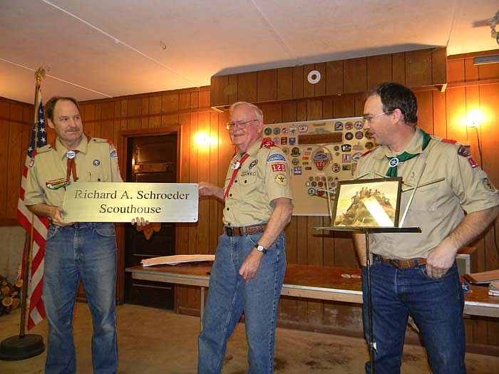 Troop 120 Assistant Scoutmaster Eric Schroeter, left, holding sign, and Scoutmaster Scott Jobe, right, honor Richard Schroeder, middle, by naming the Troop 120 scouthouse the Richard A. Schroeder Scouthouse at the Court of Honor Ceremony held Dec. 19.