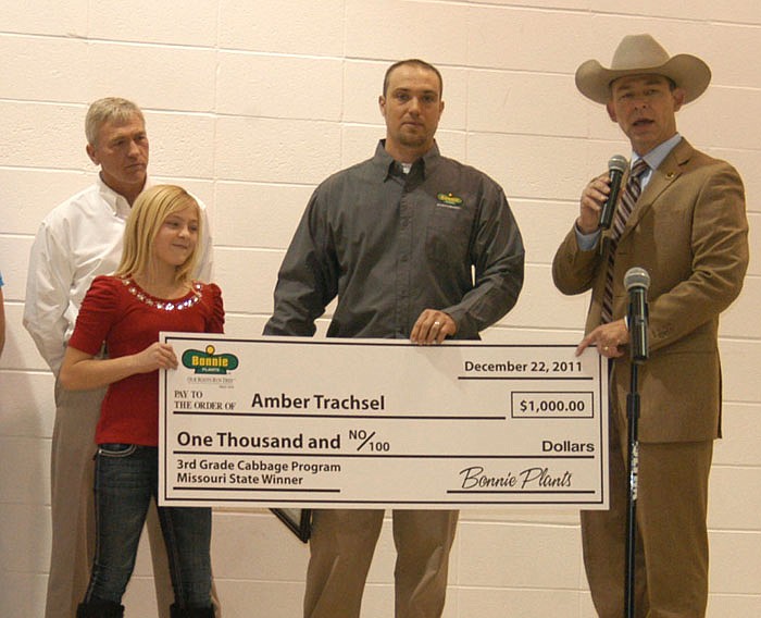 California fourth grader Amber Trachsel left, receives $1,000 Bonnie Plants scholarship check presented by B. J. Kruger, center, and Missouri Agriculture Department Director Dr. Jon Hagler, right, at the school assembly Thursday, Dec. 22. Dervin Kruger, in back, and B.J. operate the local Bonnie Plants greenhouse.