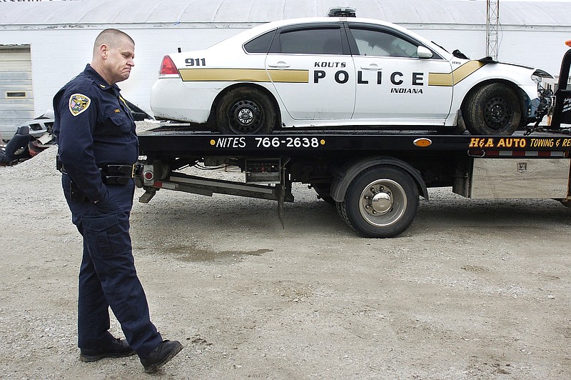 Kouts, Ind., chief James Boyce stands in front of a flatbed tow truck carrying a town police car stolen by a suspect in custody following a traffic stop Tuesday night.