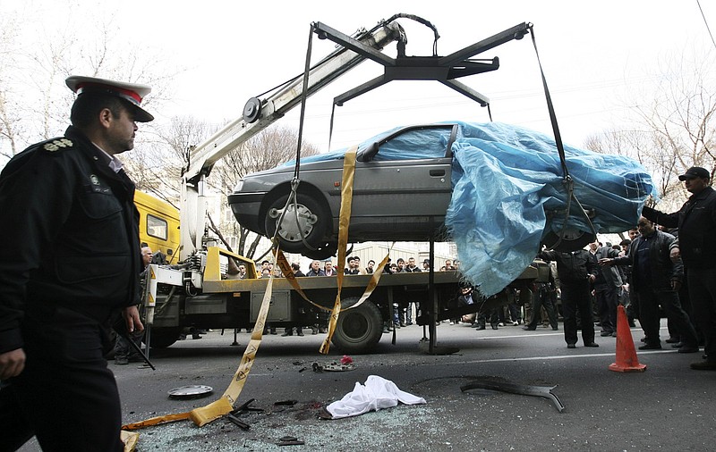 People gather around a car as it is removed by a mobile crane Wednesday in Tehran, Iran. Two assailants on a motorcycle attached magnetic bombs to the car of an Iranian university professor working at a key nuclear facility, killing him and wounding two people on Wednesday, a semiofficial news agency reported.