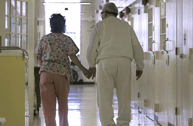 In this Wednesday, April 9, 2008 file photo, Debbie Coluter, a certified nursing assistant, holds the hand of an elderly inmate with Alzheimer's disease, as she helps him to his cell at the California Medical Facility in Vacaville, Calif. 