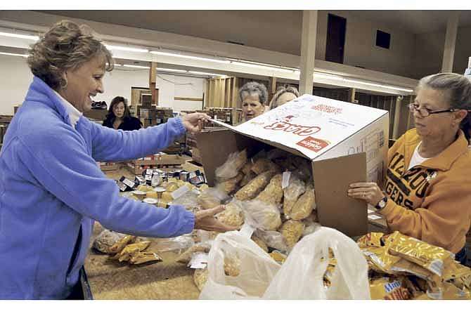 Cindy Cook catches the pre-measured bags of cereal emptied from a box by Cheri Gardner, right. The volunteers gather every Wednesday morning to fill plastic bags with food items for Buddy Packs, goodie bags that are distributed through schools for some children to take home on weekends.