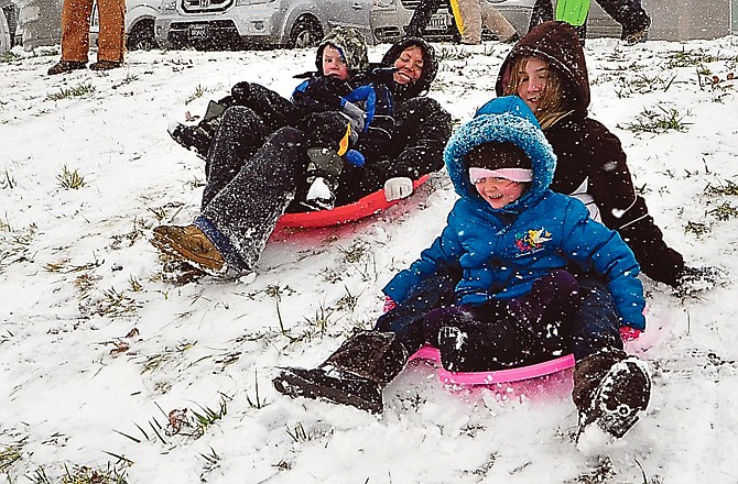 At left, the Smith family consisting of Clayton, 3, who rides with his mother, Jennifer, as Macey, 5, rides with Madison, 11, as they all slide down the hill together Monday afternoon at the hill near St. Joseph Cathedral. 
