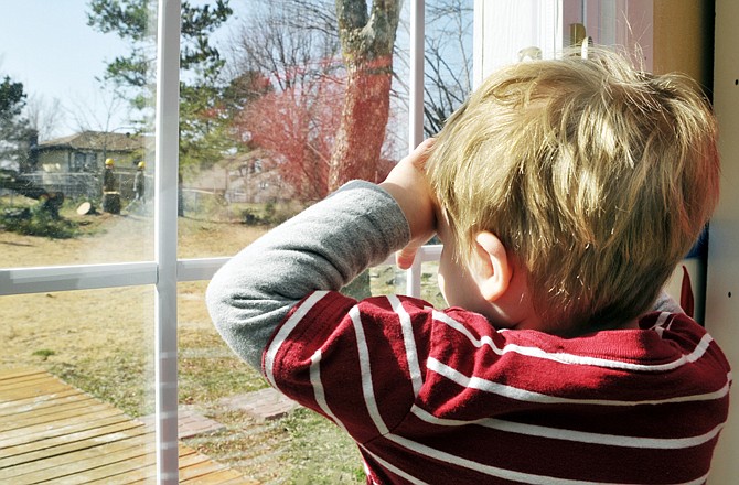 Luke Wieberg, 21â„2, watches out the sliding glass door as men in yellow hard hats cut down the tree that used to hold his swing. Through the years, it has been acceptable to have the pine tree trimmed to keep it safely out of the overhead power lines, but now the Wiebergs have been told it has to come down completely, much to Luke's dismay.