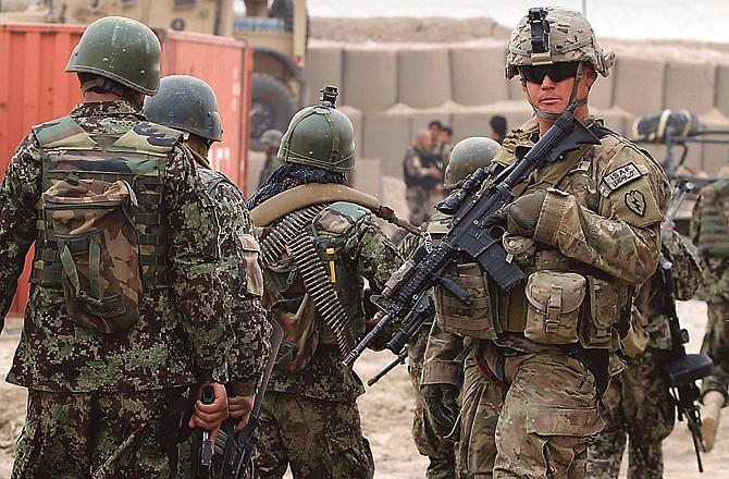 Afghan soldiers, left, walk past a watchful U.S. Army soldier outside of a military base in Panjwai, south of Kabul, Afghanistan, on Sunday. Afghan President Hamid Karzai says a U.S. service member has killed more than a dozen people in a shooting including nine children and three women. Karzai called the attack Sunday "an assassination" and demanded an explanation from the United States.