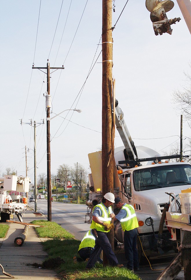 A Fulton Electric Department utility truck holds a broken electrical power line pole in place while workmen begin to install a new pole to replace the broken pole that was hit by a Fulton garbage truck Tuesday morning in front of Ovid Bell Press, 1201 North Bluff St. Traffic was blocked by downed electrical power lines.