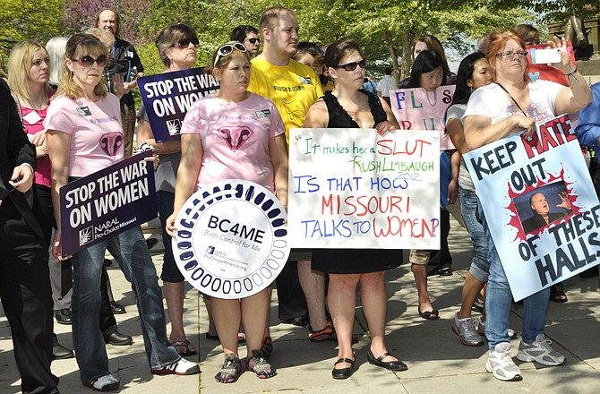 Attending an event labeled as the "Rally Against Rush and For Women's Health," several women hold signs protesting the induction of Rush Limbaugh into the Hall of Famous Missourians along with signs stating, "Stop The War On Women."