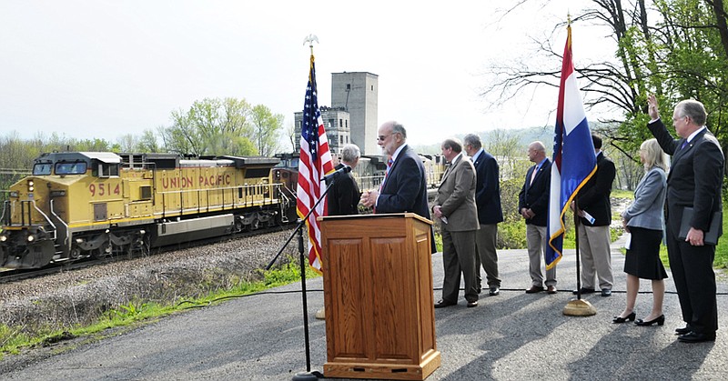 Gov. Jay Nixon, at right, waves and Tom Carper, at podium, chairman of board of directors of Amtrak, pauses from his delivery while a Union Pacific train travels through Osage City during a ground-breaking on a new railroad bridge. 