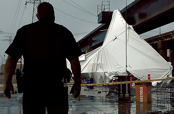 An officer from the Terminal Railroad Police Department surveys a party tent in St. Louis as it rests against a railroad trestle near a bar after storm winds blew through the area Saturday.