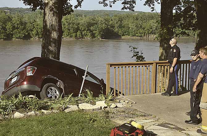 Jefferson City firefighters and police officers keep a safe distance and an eye on a vehicle and a tree as a wrecker operator (not pictured) pulls the vehicle from its position on the Missouri River bluff along Windriver Drive. The driver had been safely removed from the vehicle after she drove through the yard and hit a tree.