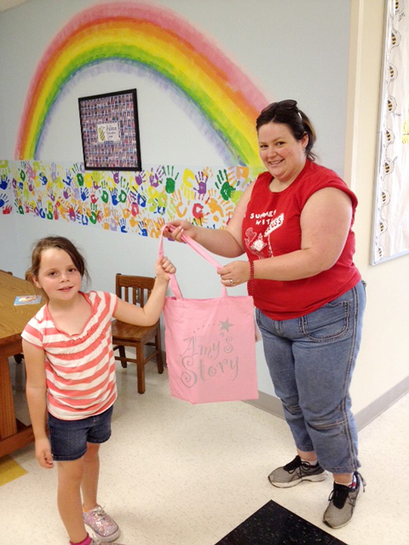 Addy Hall, along with pre-school teacher Rosalynn Strand, receives a bag stuffed with books from Amy's Story at Fulton Education Center. The literacy group donates books to children across the state of Missouri.