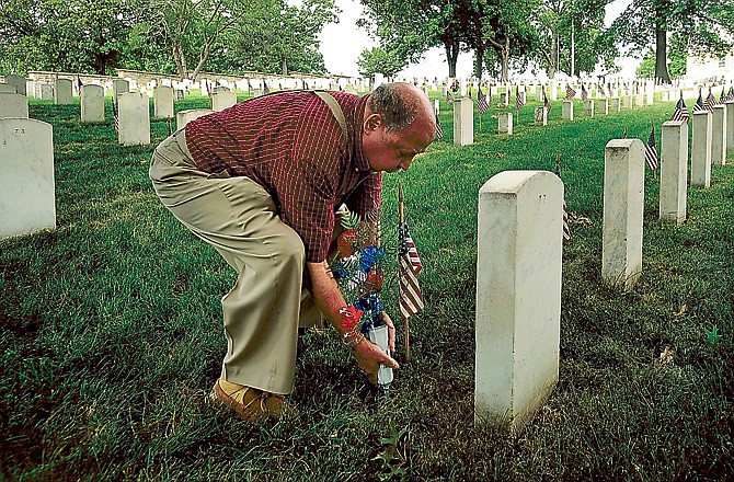 Veteran Kenneth Holman, a former U.S. Army rifleman with the 92nd Division in Italy during World War II, places flowers at the grave of his cousin, Army Sgt. Hubert Flynn Washington at the Jefferson City National Cemetery on Monday, May 25, 2015.