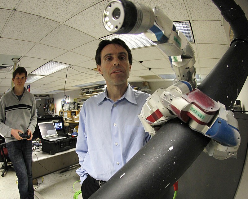 Carnegie Mellon University professor Howie Choset, right, stands beside a robot as staff researcher Florinan Enner uses a controller to demonstrate how it climbs up a tubular armature at their lab on campus in Pittsburgh. 