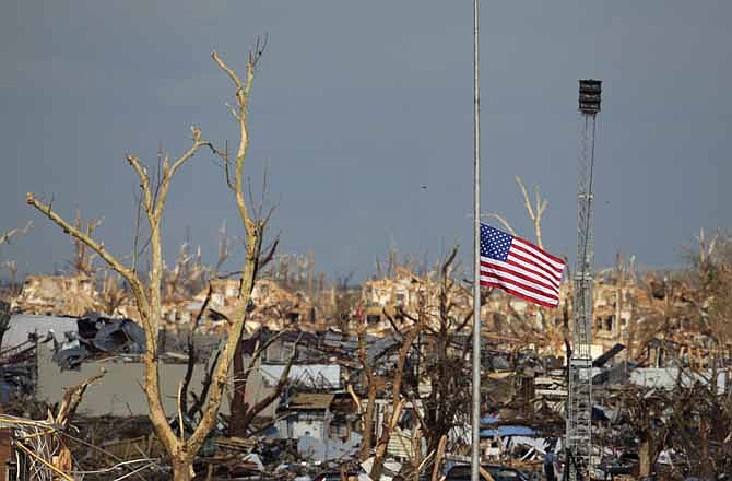 In this May 26, 2011, file photo a flag files at half staff over devastated Joplin High School next to a portable tornado siren in Joplin, Mo. Warnings sent directly to cell phones and broadcast over the airwaves can provide a detailed heads-up before dangerous storms, but through many parts of Tornado Alley, storm sirens remain so ubiquitous that one official says the pole they sit on almost could be called the state tree of Kansas.