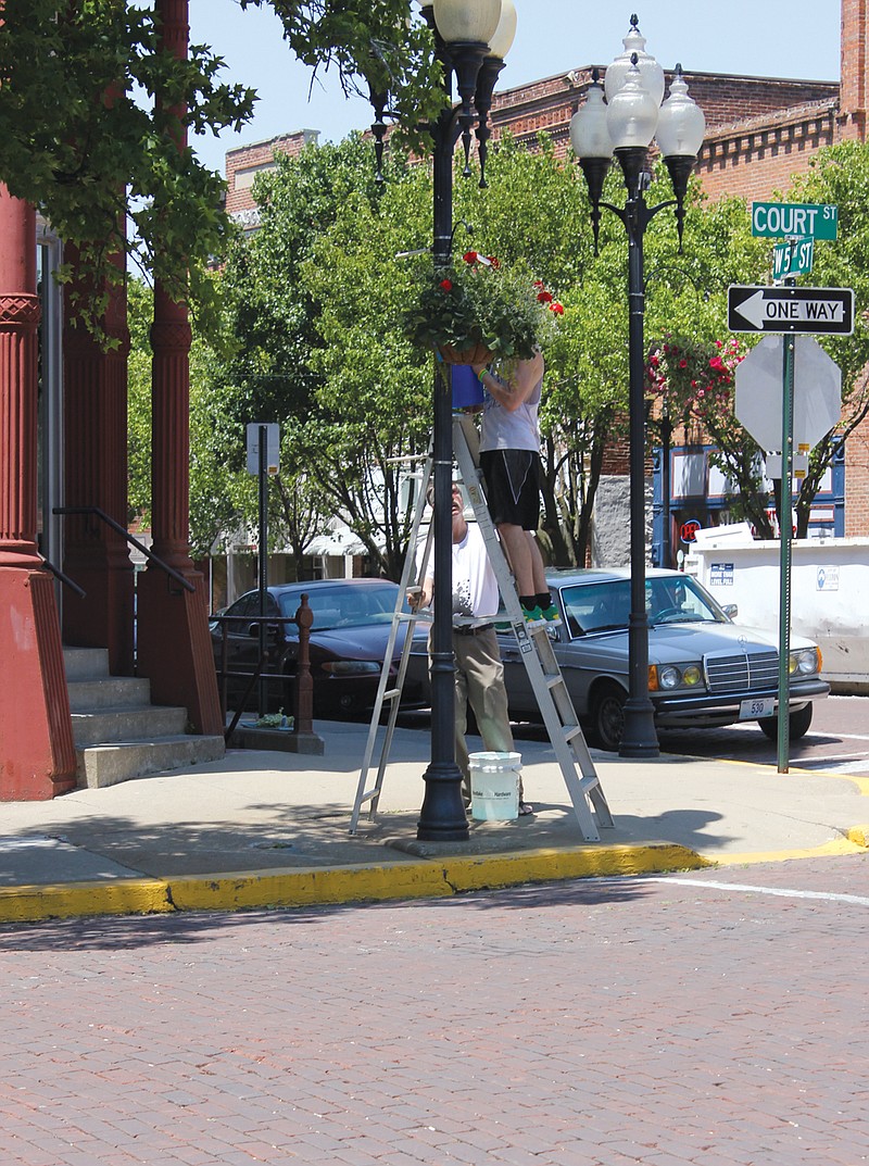 FULTON SUN file photo
Workers water one of the hanging flower arrangements recently near Court and 5th streets. The City Council is looking for volunteers to help water the flowers.