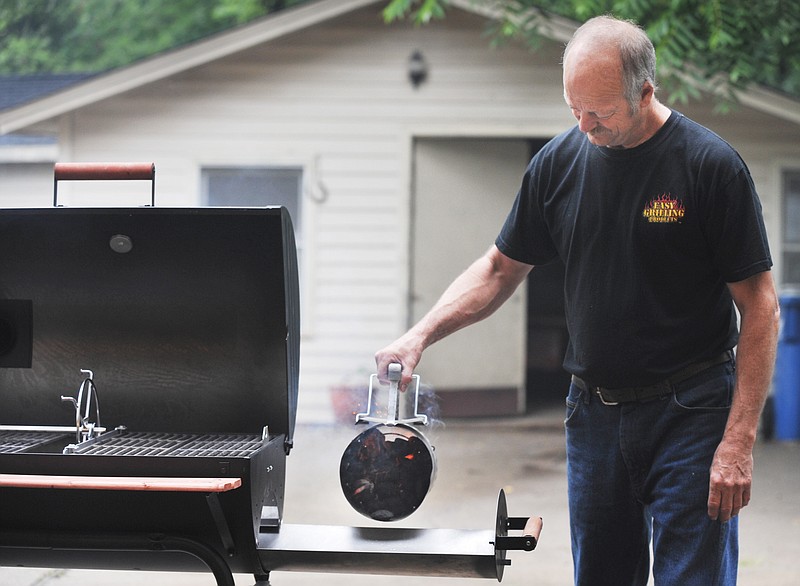 Harvey Toebben pours hot charcoal into the pull-out charcoal tray on a grill modified by Easy Grilling Products of Jefferson City. They purchase grills that are available from a number of outlets locally and modify them for resale. The slide out charcoal tray has been a hit with avid grillers.