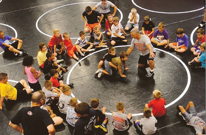 Young campers circle up in the Jays Wrestling Room to watch a demonstration on proper restart positions during the final day of the Jefferson City wrestling camp Friday.