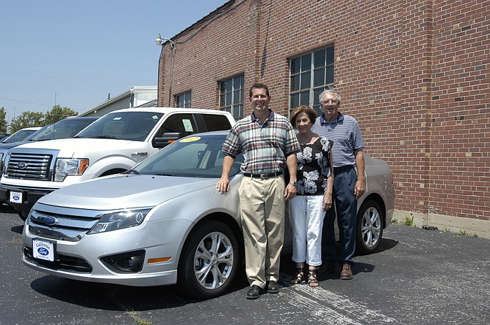 From left, owner and Dealer Principal Steve Sakelaris, owner Mary Sakelaris and former owner/dealer Larry Schenewerk with a new Ford Fusion after completing the documentation necessary to transfer the dealearship to the new owners. 