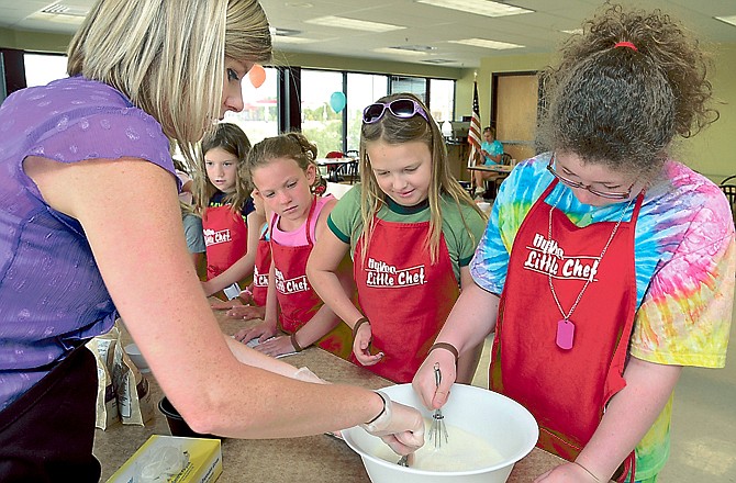 Lindsey Koelling, a registered dietician with Hy-Vee, works with youngsters during the last session of Hy-Vee Kids Summer Camp. They were making a dairy dessert of white chocolate mousse with berries. Macy Kopp stirs the mix as Jadan Crader and Kyndel Bickel wait for their turn to stir