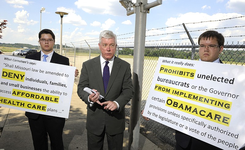 Lt. Gov. Peter Kinder is flanked Tuesday by staff members holding signs with ballot language written by Secretary of State Robin Carnahan, left, and Kinder's interpretation of the ballot language, right. Kinder filed a lawsuit against Carnahan and Attorney General Chris Koster accusing Carnahan of deceptive ballot language.