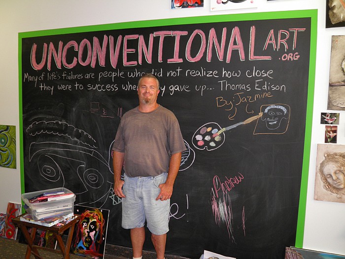 Stephen R. Feilbach, inside the Unconventional Art studio, stands in front of a chalkboard where people of all ages are encouraged to draw and express themselves.