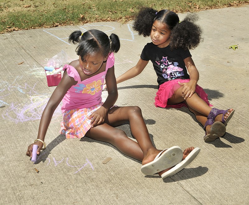 Kaylee Ware, left, and Serenity Moore, 7, use chalk to draw on the sidewalk as they wait for the Food 4 Kids sandwiches to arrive. Since mid-July, staff from the YMCA have gone to the parks where volunteers from the Food 4 Kids program deliver lunches for neighborhood youngsters. While there, the children are encouraged to exercise and get moving, even if just for a little while.