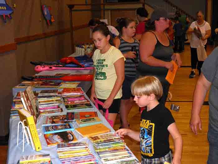 Participants in the Wood Place Public Library Summer Reading Club check out books to purchase with tickets earned over the summer at the "Out of this World" Party held Thursday, Aug. 2, at California United Church of Christ.