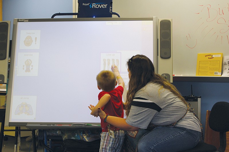 Rosalynn Strand helps a student drag a visual schedule across one of Fulton Education Center's new smart boards Wednesday. The boards are just some of the technology that FEC is using to help teach preschoolers across all ages and development levels.