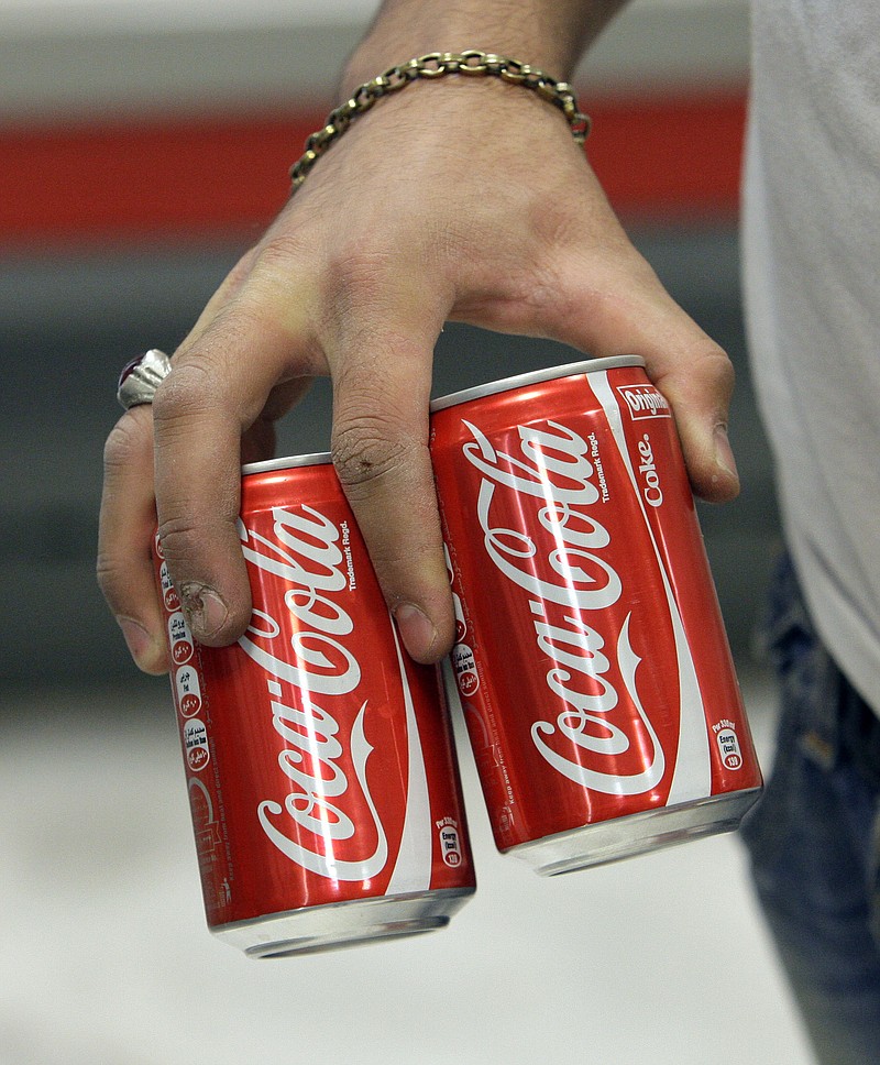 Iranian worker Mahmoud Kouhi carries two cans of Coca-Cola, in a grocery store in Tehran, Iran. Even after decades of diplomatic estrangement and tightening economic sanctions, American products find their way to the Islamic Republic through back channel exporters, licensing workarounds and straightforward trade in goods not blocked by U.S. embargoes.