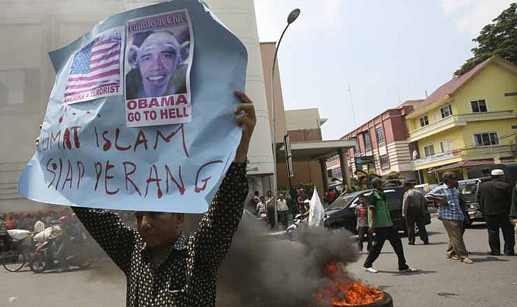 An Indonesian Muslim holds up a poster as a tire burns during a protest against an American film that ridicules Prophet Muhammad outside the U.S. Consulate in Medan, North Sumatra, Indonesia, Tuesday, Sept. 18, 2012. Indonesians continue to protest the anti-Islam film "Innocence of Muslims," torching the flag and tires outside the consulate in the country's third largest city of Medan. The poster reads: "Muslims are ready for war."