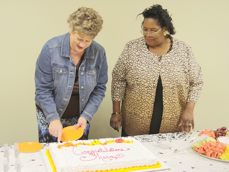 Librarian Julie Murphy (left) slices cake during the 35th anniversary party for Sherry McBride-Brown (right) Friday afternoon.