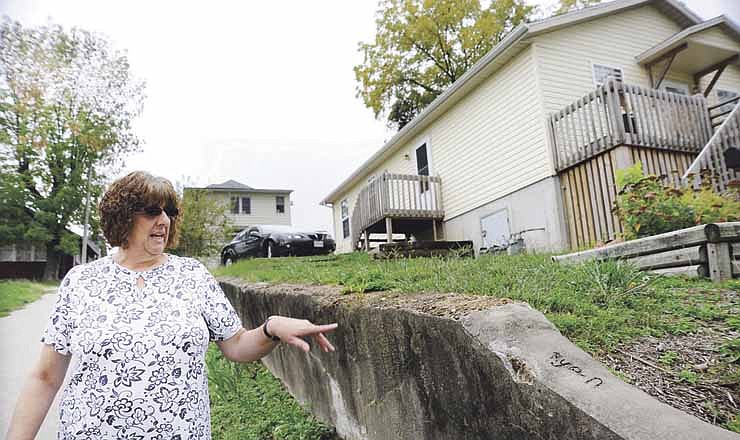 Homeowner Debbie Hall points out her son Ryan's name Thursday on a retaining wall which needs to be replaced. Hall will receive help from a new program called A Brush with Kindness which is designed to help low-income homeowners with repair projects.