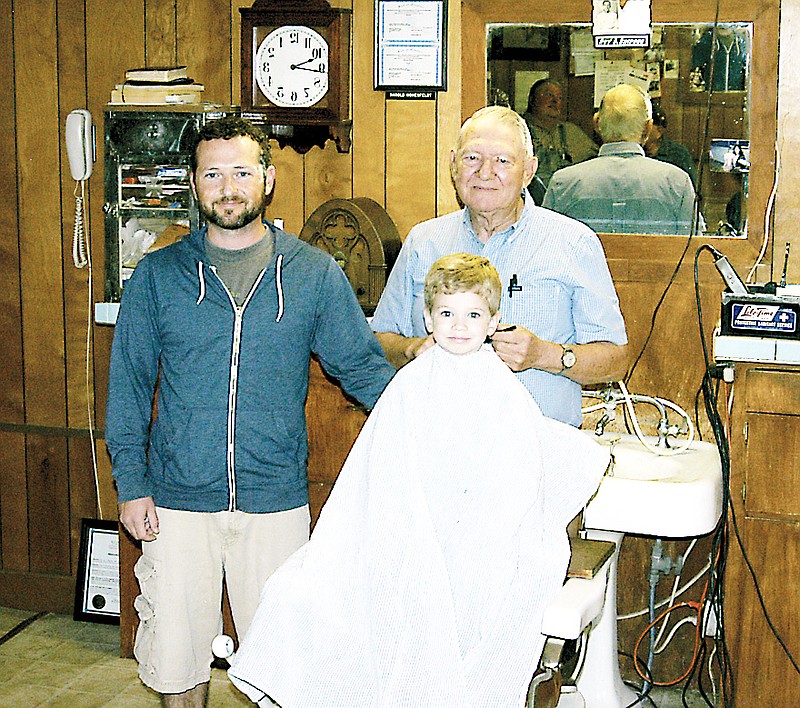 Willis Lehman, on the longtime booster board in the barber chair with his great-grandfather Roy Dean Simpson ready to trim. Willis's dad and Simpson's grandson Jonathan Lehman stands by.  