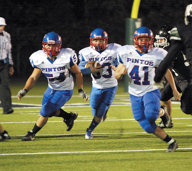California's Seth Fairchild, center, gains yards as Curtis Fulks, left, and Luke Burger, right, help pave the way during Friday night's varsity football game at Warsaw. The Pintos defeated the Wildcats 44-7.