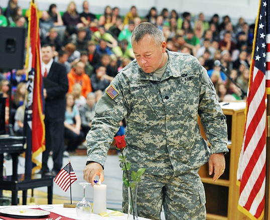 Before starting his presentation, Missouri Army National Guard Lt. Col. John Jurgensmeyer lights a single candle at the MIA/POW table set up for the Veterans Day assembly at Blair Oaks High School. 