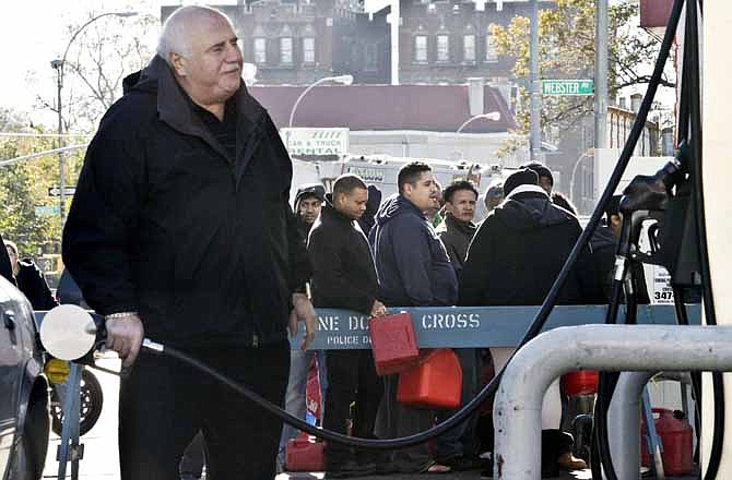 A motorist pumps gas while people stand in line with containers to purchase gas on Friday, Nov. 9, 2012 in Brooklyn, N.Y. Police were at gas stations to enforce a new gasoline rationing plan that lets motorists fill up every other day that started in New York on Friday morning.