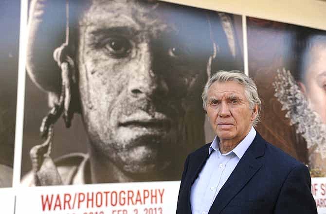 In this Thursday, Nov. 8, 2012 photo, photographer Don McCullin poses in front of the Houston Museum of Fine Arts' sign promoting the new War/Photography exhibit in Houston. The exhibit displays the work of 280 photographers from 28 nations covering the Mexican-American war in 1846 to present-day. McCullin has four photos in the exhibit.