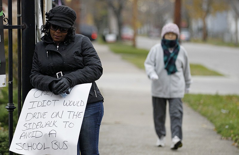 A woman walks by as Shena Hardin, left, holds up a sign to serve a highly public sentence Tuesday in Cleveland. Hardin was caught on camera driving on a sidewalk to avoid a Cleveland school bus that was unloading children.  A Cleveland Municipal Court judge ordered 32-year-old Hardin to serve the highly public sentence for one hour Tuesday and Wednesday.