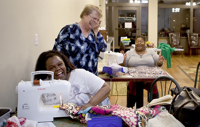From left, Latonya Kornegay, Debbi Fletcher and Tamara Pitts share a laugh after Fletcher unplugged a machine that kept uncontrollably speeding up Thursday night. Fletcher is one of two instructors of a beginners level sewing class held at Common Ground Community Center.