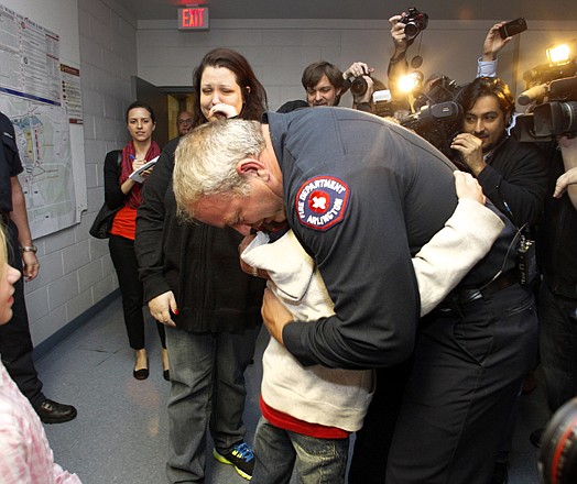 Rebecca Quintanilla, center left, wipes tears from her face as her adopted son Koregan, 10, hugs Arlington Fire Fighter Wesley Keck, center right, as the two meet Thursday, in Arlington, Texas. 