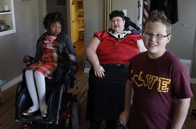 In this Nov. 14, 2012 photo, Carrie Ann Lucas, center, sits with her adopted daughter, Adrianne, 13, as her adopted son Anthony, 11, walks past them as he gets himself ready in the morning, at their home in Windsor, Colo. Carrie Ann Lucas uses a power wheelchair and is reliant on a ventilator due to a form of muscular dystrophy. She is a single mother of four adopted children, ages 22, 17, 13 and 11, all of whom also have disabilities, including two who use wheelchairs and three with intellectual disabilities.
